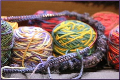 Lots of stitches cast on to the knitting needles, among a pile of small balls of yarn
